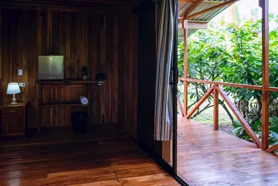 a room with a wooden floor and a balcony with a television at Río Celeste, Cacahua Lodge in Rio Celeste
