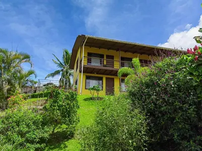 a yellow house with trees and bushes at Hotel Aurora Inn, Nuevo Arenal in Nuevo Arenal