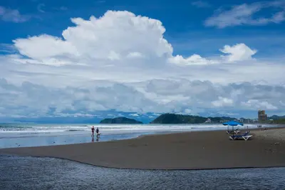 two people standing on a beach with an umbrella at Jaco Laguna Resort & Beach Club in Jacó
