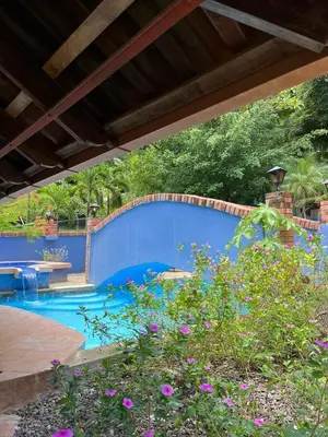 a swimming pool with a blue fence and flowers at Siwõ Art Guesthouse in Ocotal