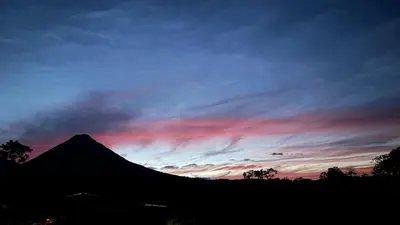 a silhouette of a mountain with a sunset in the sky at Arenal Monara in Fortuna