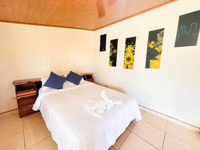 a bedroom with a bed with white sheets and pictures on the wall at Kiwi House in Monteverde Costa Rica