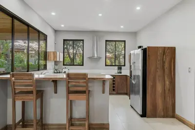 a kitchen with a stainless steel refrigerator and wooden stools at Stylish 3-Bedroom Tropical Escape with Pool & Outdoor Living, 1 Block from Playa Potrero in Potrero