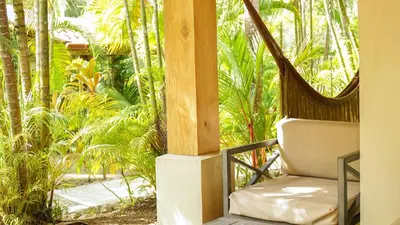 a hammock chair sitting on a porch with palm trees at Playa Cielo Beachfront Hotel - Santa Teresa, Costa Rica in Santa Teresa Beach
