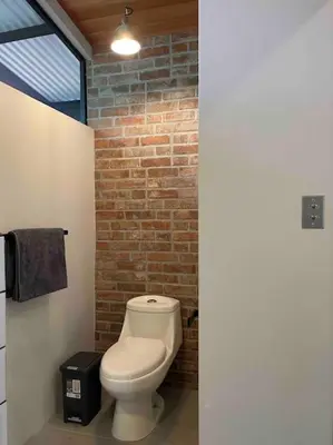 a bathroom with a toilet and a brick wall at Industrial Studio with private Jacuzzi in Uvita