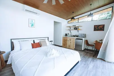 a bedroom with a large white bed and a kitchen at Natura Bungalows in Fortuna