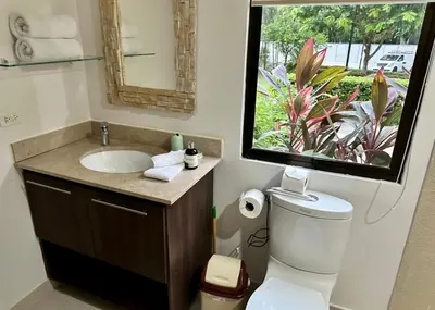a bathroom with a toilet and a sink with a window at Private Modern Condo by Jac Beach in Jacó