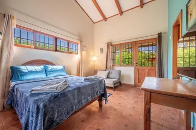 a bedroom with a bed and a chair and windows at Casa Palma Real in Playa Junquillal