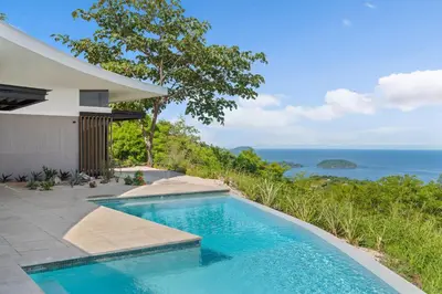 a swimming pool in front of a house with the ocean at Luxurious Ultramodern Property with Private Suites, Infinity Pool, and Sweeping Ocean and Mountain Views in Potrero
