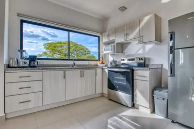 a kitchen with white cabinets and a large window at Muna Santa Rosa Apartamentos in Tamarindo