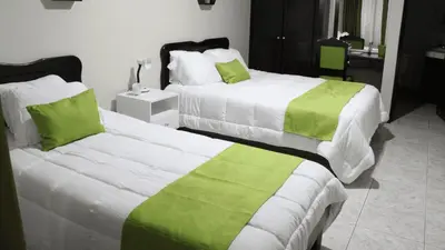 two beds in a hotel room with green and white sheets at Hotel América Heredia in Heredia
