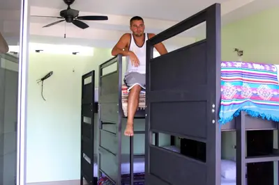 a man sitting on top of a bunk bed at Room2Board Hostel and Surf School in Jacó