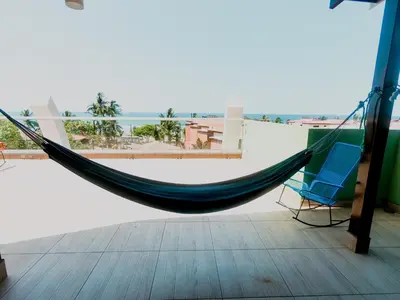 a hammock and a chair on a balcony at Room2Board Hostel and Surf School in Jacó