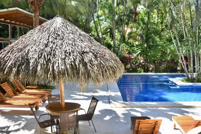 a table with a straw umbrella next to a swimming pool at Fuego Lodge in Santa Teresa Beach
