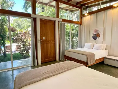 two beds in a room with large windows at Fuego Lodge in Santa Teresa Beach