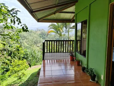a green house with a balcony with potted plants at Bella Vista Guest house in Turrialba