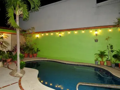 a pool with a green wall with palm trees and lights at Hotel La Guaria Inn & Suites in Alajuela City