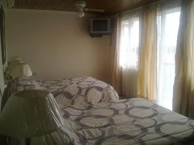 a bedroom with a bed and a lamp and windows at Hotel La Guaria Inn & Suites in Alajuela City