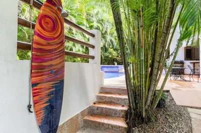 a surfboard leaning against a wall next to a palm tree at Dreamcatcher Hotel - Live the Dream of Santa Teresa in Santa Teresa Beach