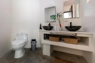 a bathroom with a white toilet and two sinks at Private pool & rooftop patio Hot tub, AC, WI-FI in Jacó