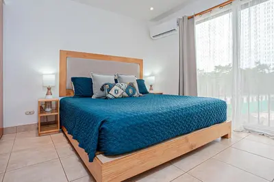 a bedroom with a bed with a blue comforter and a window at Palmas de Tamarindo 201D in Tamarindo