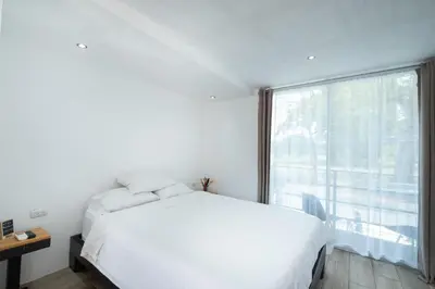 a bedroom with a white bed and a large window at Hotel Bamboo in Jacó