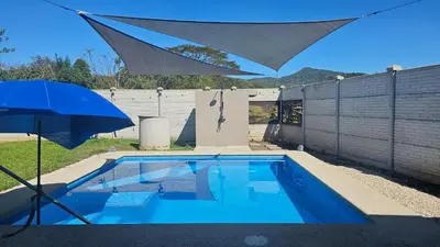 a blue swimming pool with an umbrella next to a fence at Beautiful modern house in Nandayure