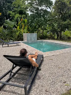 a woman sitting in a chair next to a swimming pool at Villas Sapiens Arenal in Fortuna