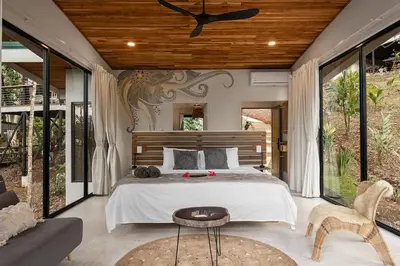 a bedroom with a bed and a table and some windows at Pandanus Lodge & Retreats Bungalow Gingiber in Cariblanco