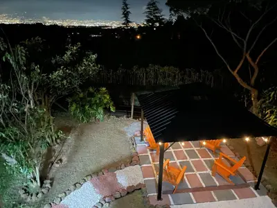 a patio with two orange chairs and a black umbrella at Parque Nacional Volcán Poás Cabaña Abby in Bajos Tigre