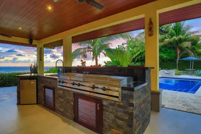 an outdoor kitchen with a grill and a swimming pool at Ojochal Magnificent Ocean View in Ojochal