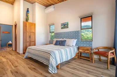 a bedroom with a bed and a chair and windows at Villa Roca Ocean to Mountain Views - by Pura Villas in Ojochal