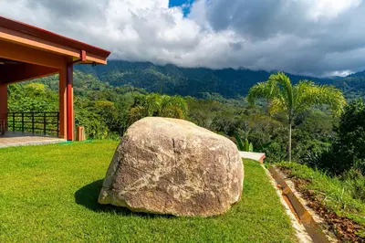 a large rock sitting in the grass next to a building at Villa Roca Ocean to Mountain Views - by Pura Villas in Ojochal