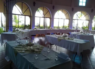 a row of tables with wine glasses in a room with windows at Hotel Delfin Playa Bejuco in Esterillos Este
