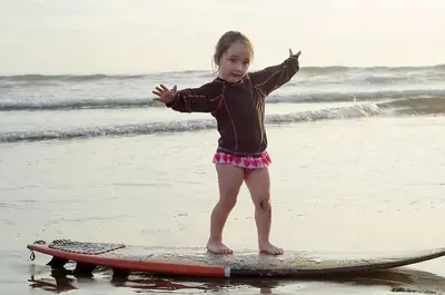 a little girl standing on a surfboard on the beach at Hotel Delfin Playa Bejuco in Esterillos Este