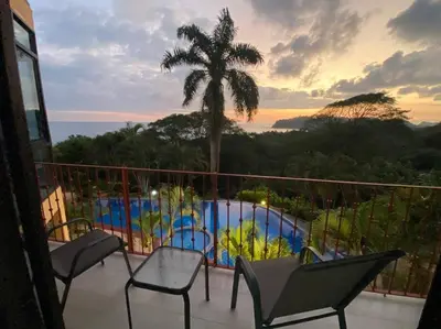 a balcony with chairs and a palm tree and a pool at Modern condo with stunning ocean views in Samara in Sámara