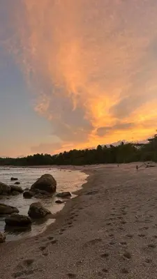 a sunset on a beach with rocks in the water at Anez Cabin'S in Cabuya