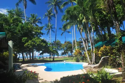 a swimming pool next to a beach with palm trees at Rafiki Beach Camp in Matapalo