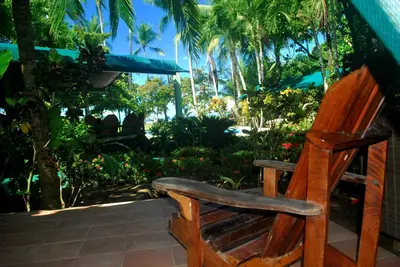 a wooden chair sitting on a patio with palm trees at Rafiki Beach Camp in Matapalo