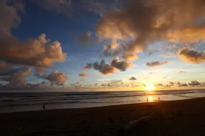 a sunset on the beach with people walking on the beach at Rafiki Beach Camp in Matapalo