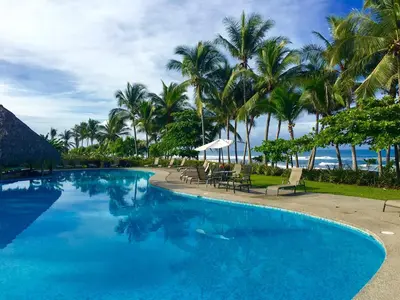 a large swimming pool with palm trees and the ocean at Modern Beachfront Paradise - Hermosa Palms 8 in Playa Hermosa