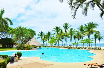 a swimming pool with palm trees and a beach at Luxury Beachfront Oasis - Hermosa Palms 50 in Playa Hermosa