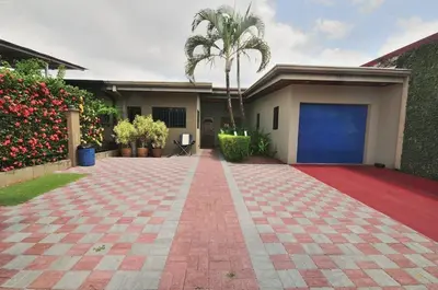 a house with a palm tree and a red brick driveway at Casa Suenos- Iconic 4BR Home with Private Pool in Jacó