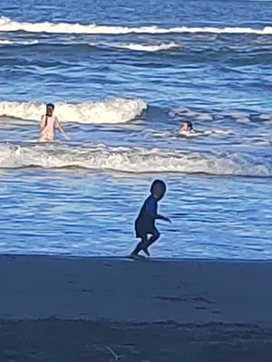 a child walking on the beach with people in the ocean at Cabinas Agamy in Tortuguero