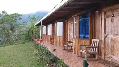 a wooden cabin with chairs and a table on the porch at Mirador Valle del General in La Ese