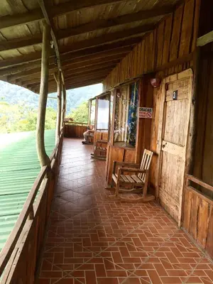 a porch of a wooden cabin with a chair and water at Mirador Valle del General in La Ese