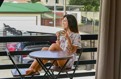 a woman sitting on a balcony drinking a cup of coffee at Rooftop and stunning Arenal Volcano views 3 minutes from La Fortuna in Fortuna