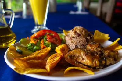 a plate of food with meat and chips and a drink at Cabinas El Muellecito in Tortuguero