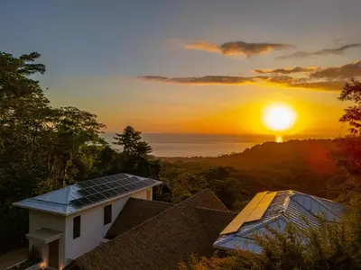 a sunset over a house with solar panels on the roof at Casa Frenchie - by Pura Villas in Dominicalito