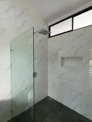 a glass shower in a bathroom with white marble walls at Toucan home in Fortuna